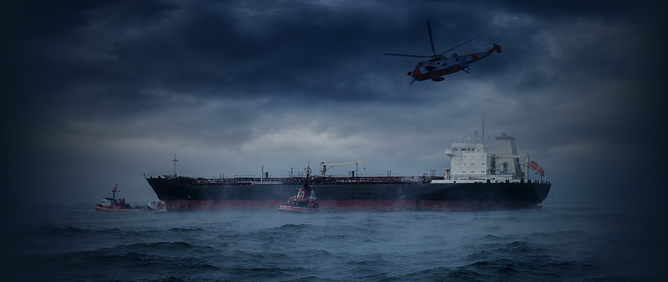 The image shows a stormy sea scene with a large tanker ship and a couple of tugboats, under dark clouds. A red and white helicopter hovers nearby, suggesting a rescue or emergency operation.